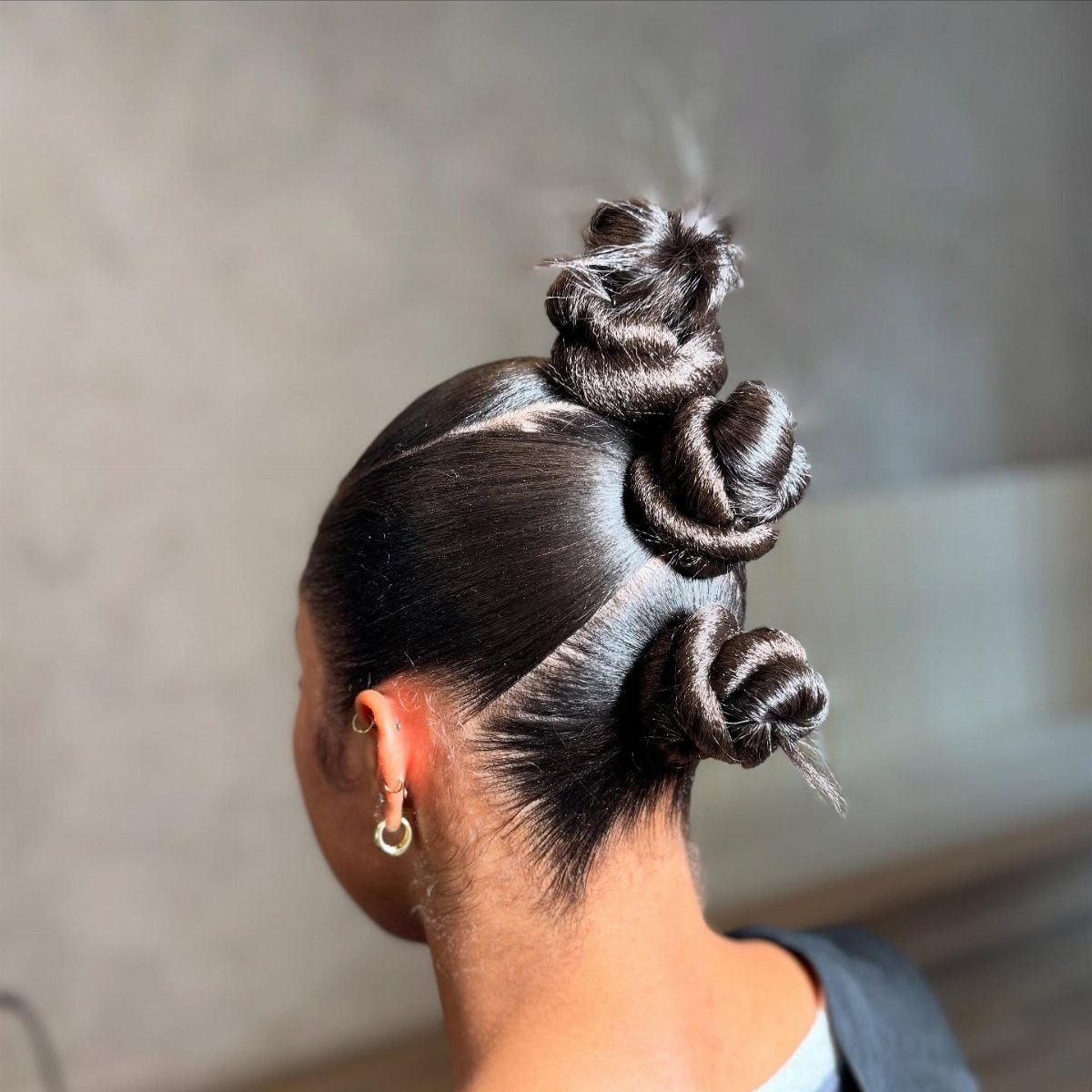 Three glossy coiled hair knots arranged down the back of a slicked hairstyle