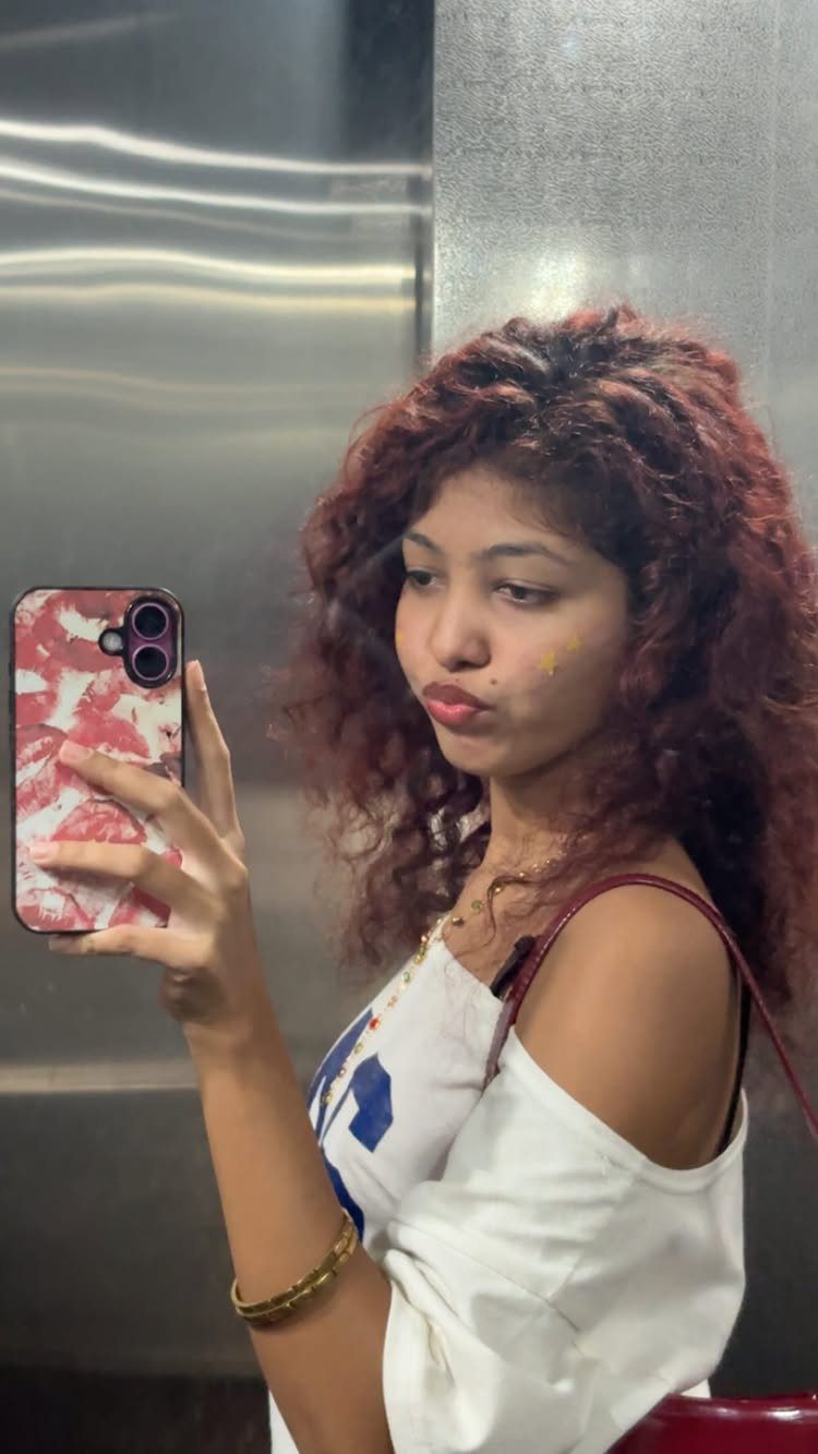 Woman showing voluminous deep burgundy-red curly hair in an elevator mirror selfie