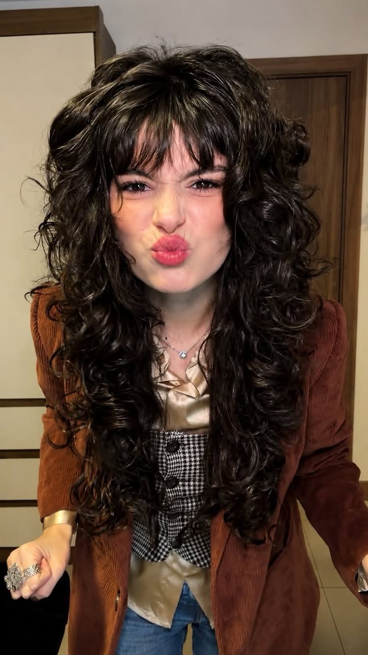 Person posing with long dark curls and bangs framing the forehead