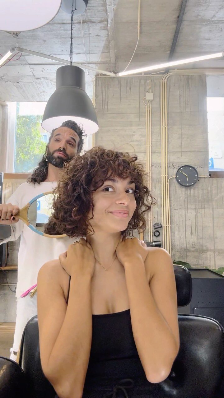 Woman showing a chin-length curly bob in a bright salon