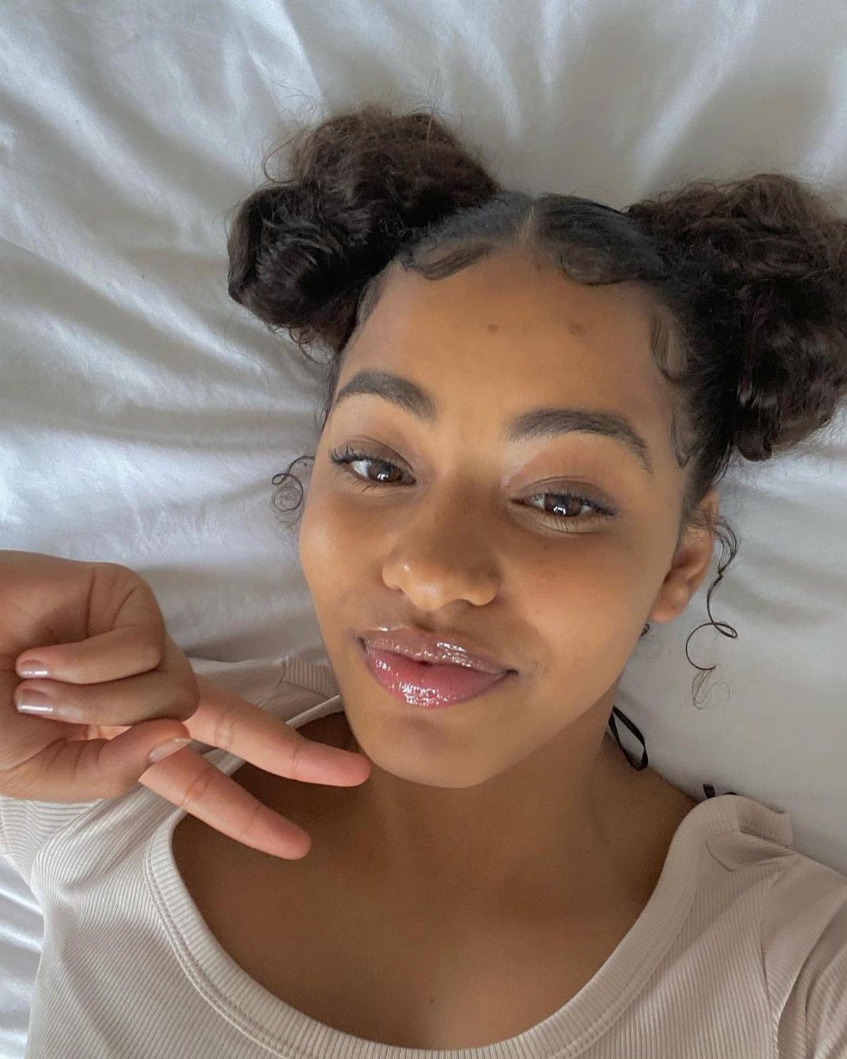 Woman with curly hair in two buns lying on white bedding