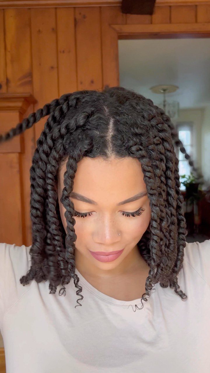 Dark two-strand twists frame a person's face, ending in loose curls