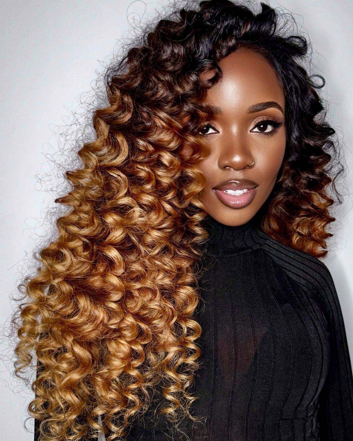 Woman displaying long ombré curls with dark roots and golden brown ends