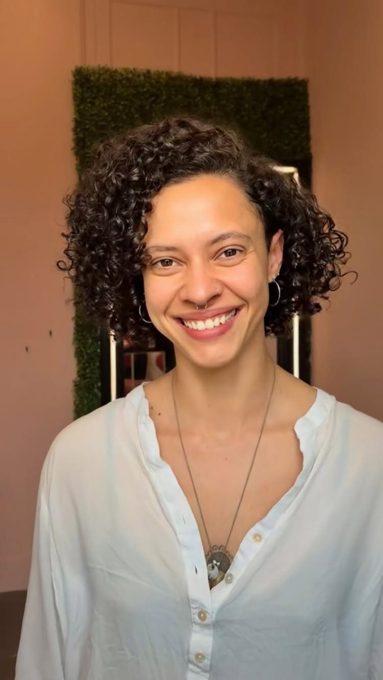 Woman with rounded, layered dark curls smiling in a pale blue blouse