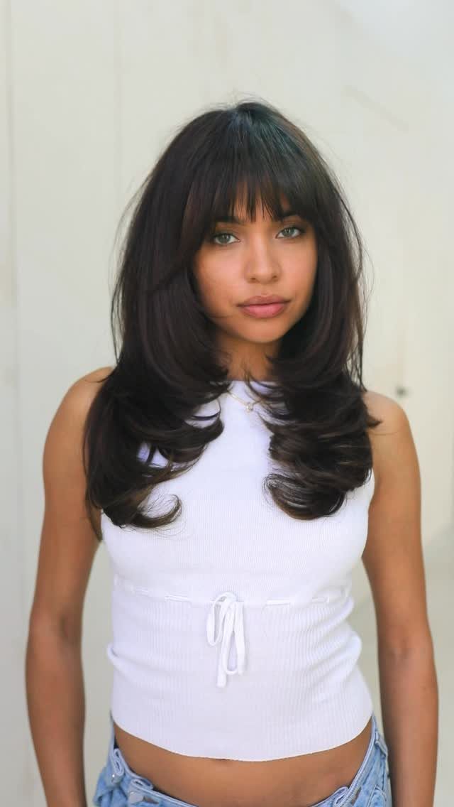 Woman with dark bangs and long, bouncy layers curled inward at the ends
