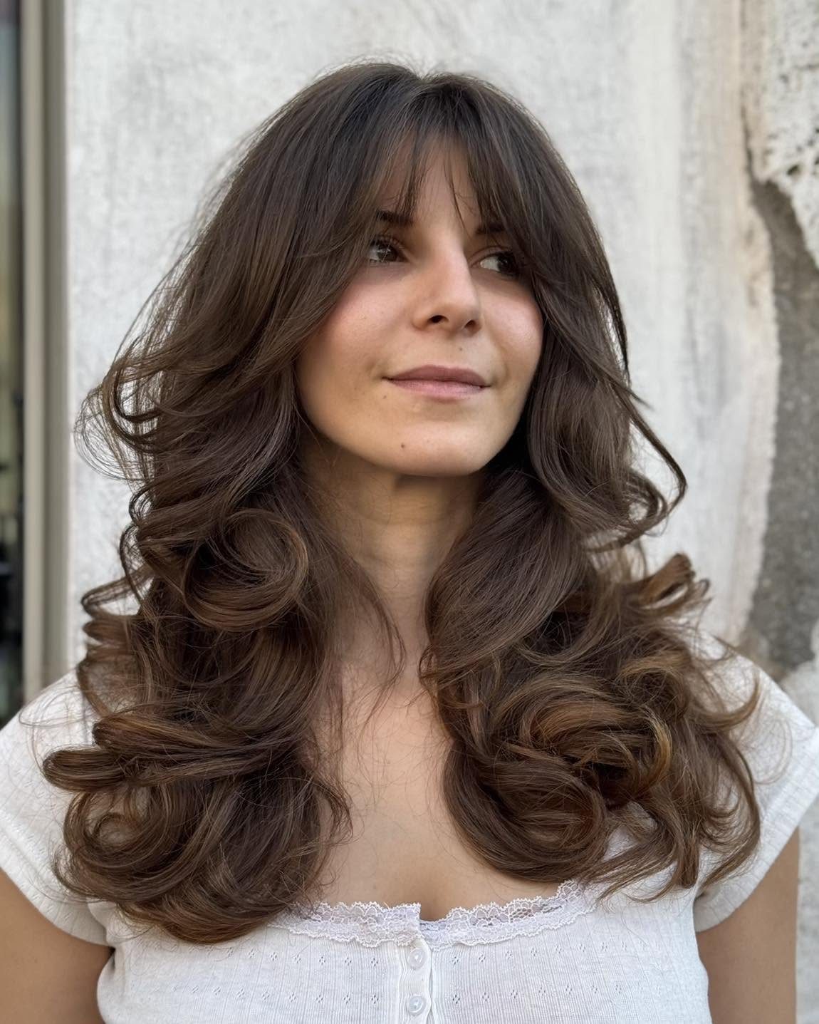 Woman with long brown face-framing layers and a tapered center-parted fringe
