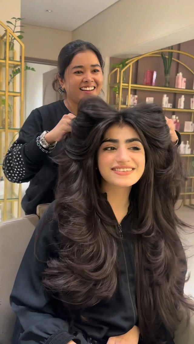 Long-haired woman displays voluminous butterfly layers and bangs in a salon