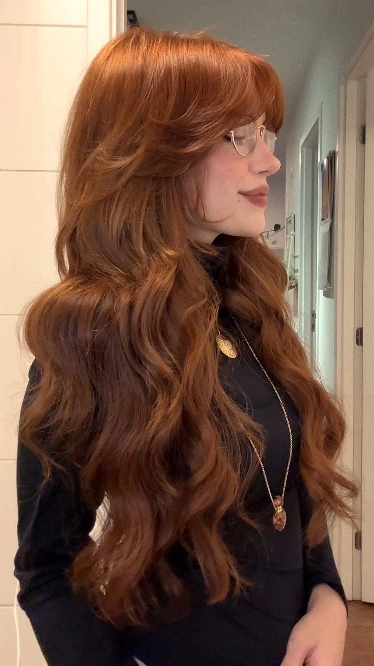 Woman with thick, long auburn waves and sweeping bangs framing her face