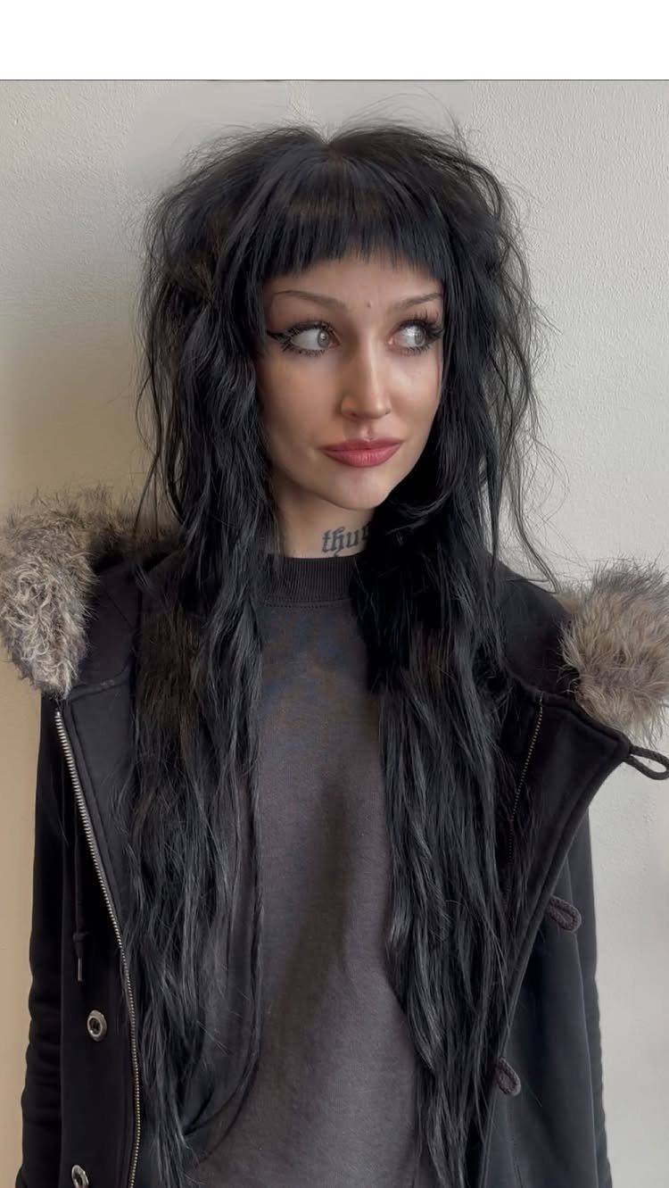 Woman with long dark layers and straight bangs wearing a black jacket