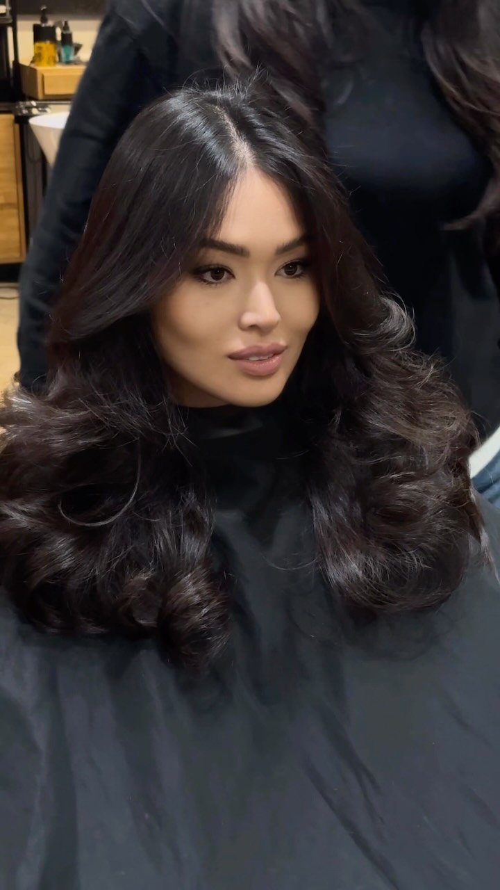 Woman with long dark layered hair styled in voluminous soft waves at a salon