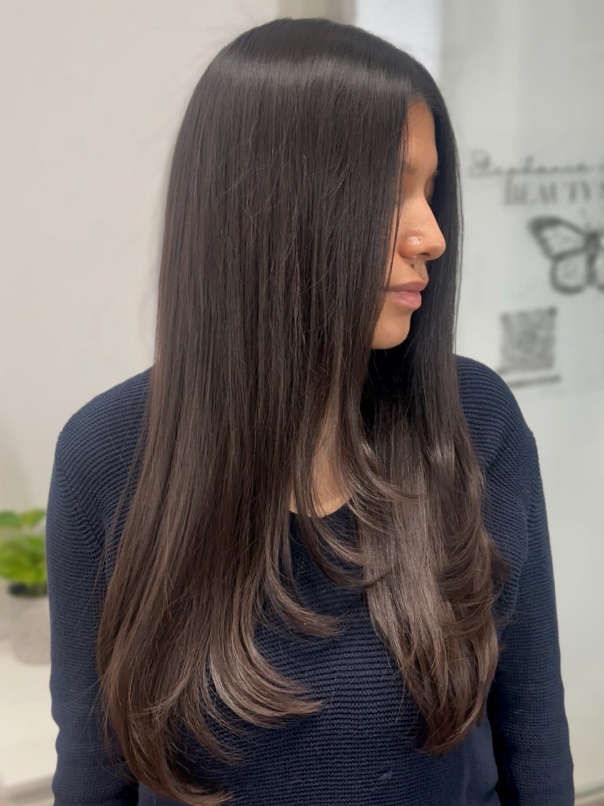 Woman showing long, sleek dark hair with subtle layers and curved ends