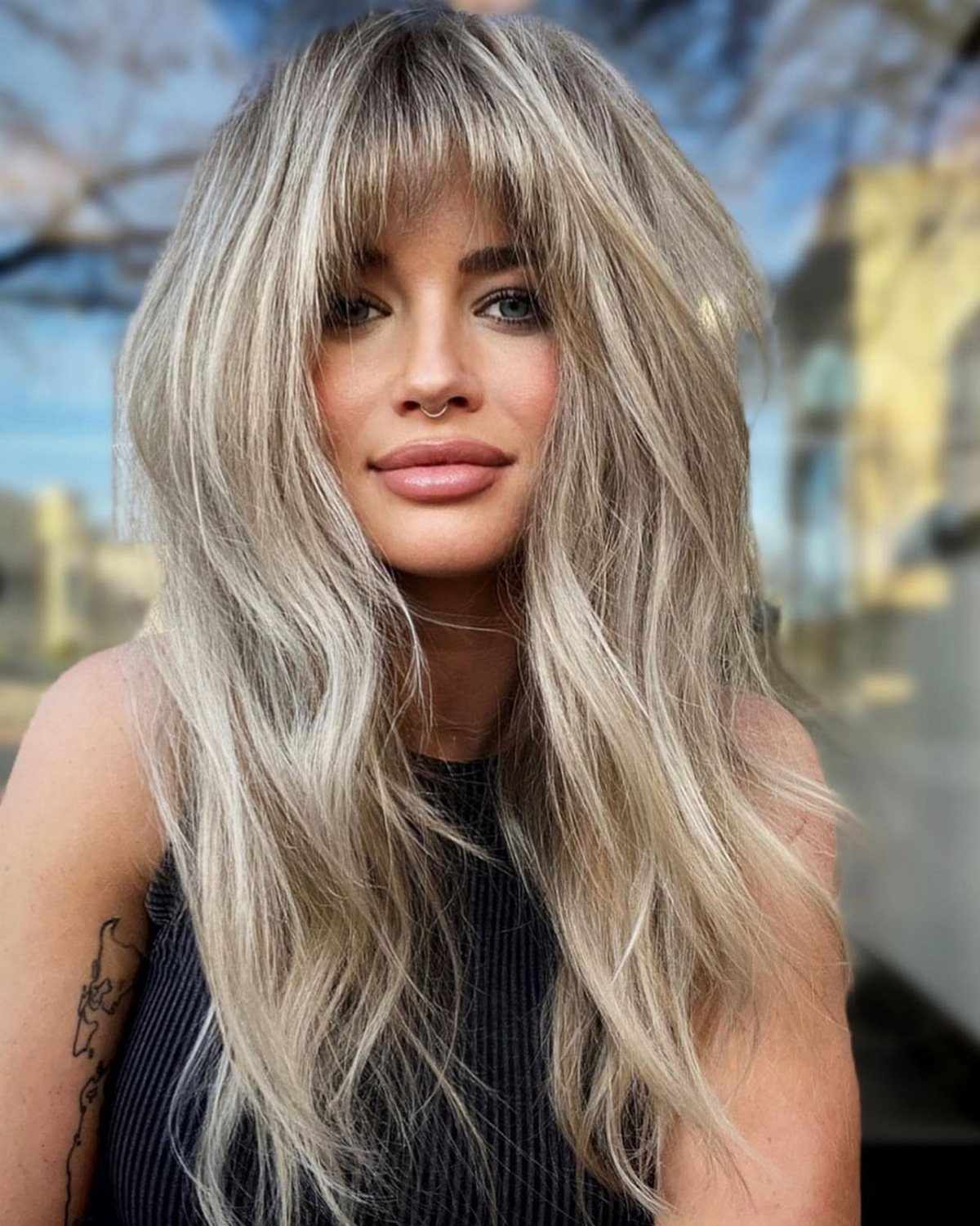 Woman with long ash-blonde layers and softly rounded bangs framing her face