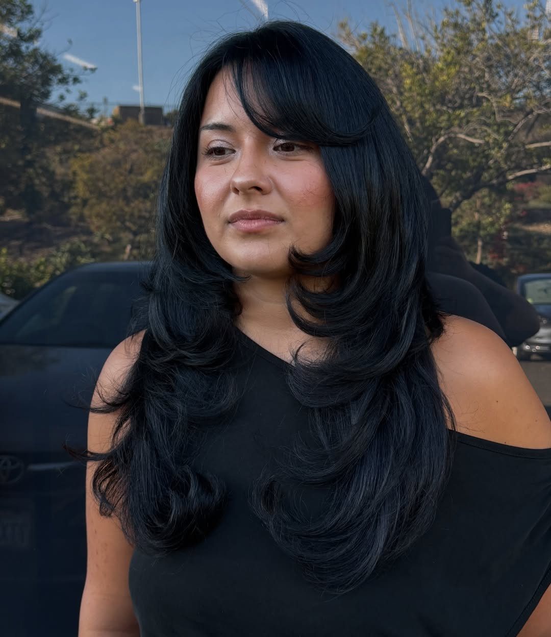 Woman with long dark layered hair and a sweeping fringe across her forehead