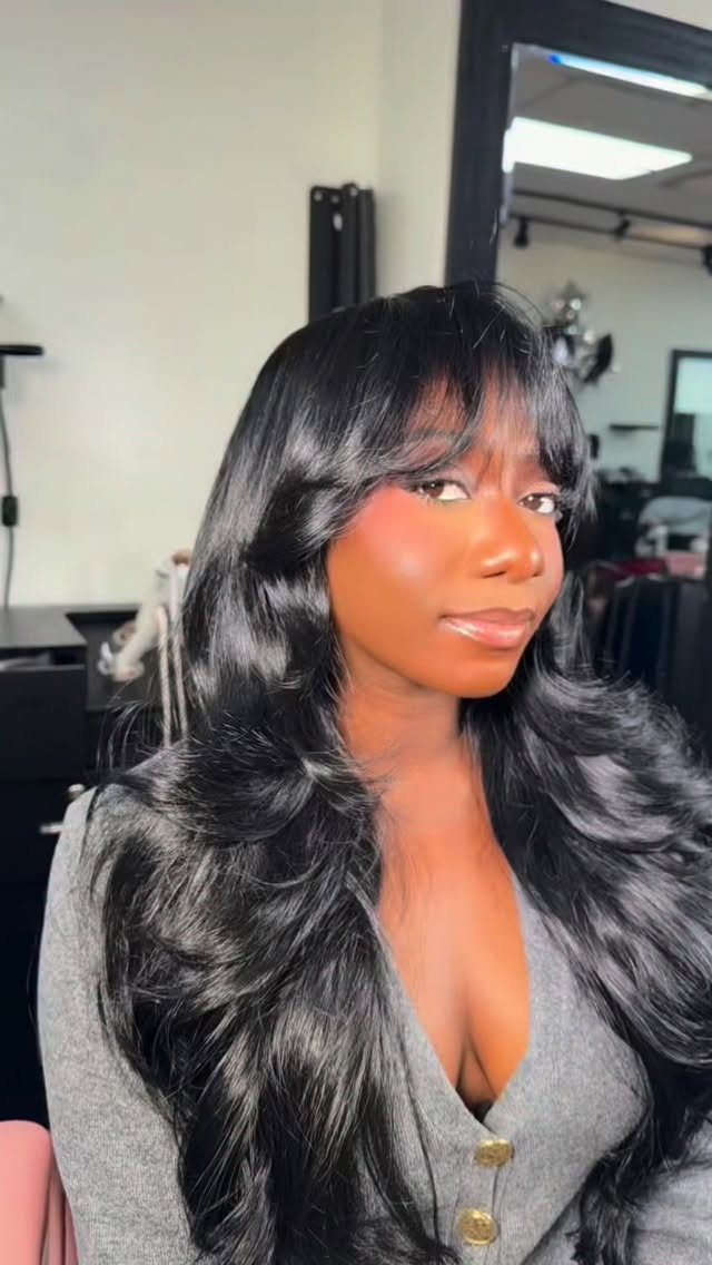 Woman showing long layered black hair with wispy bangs in a salon