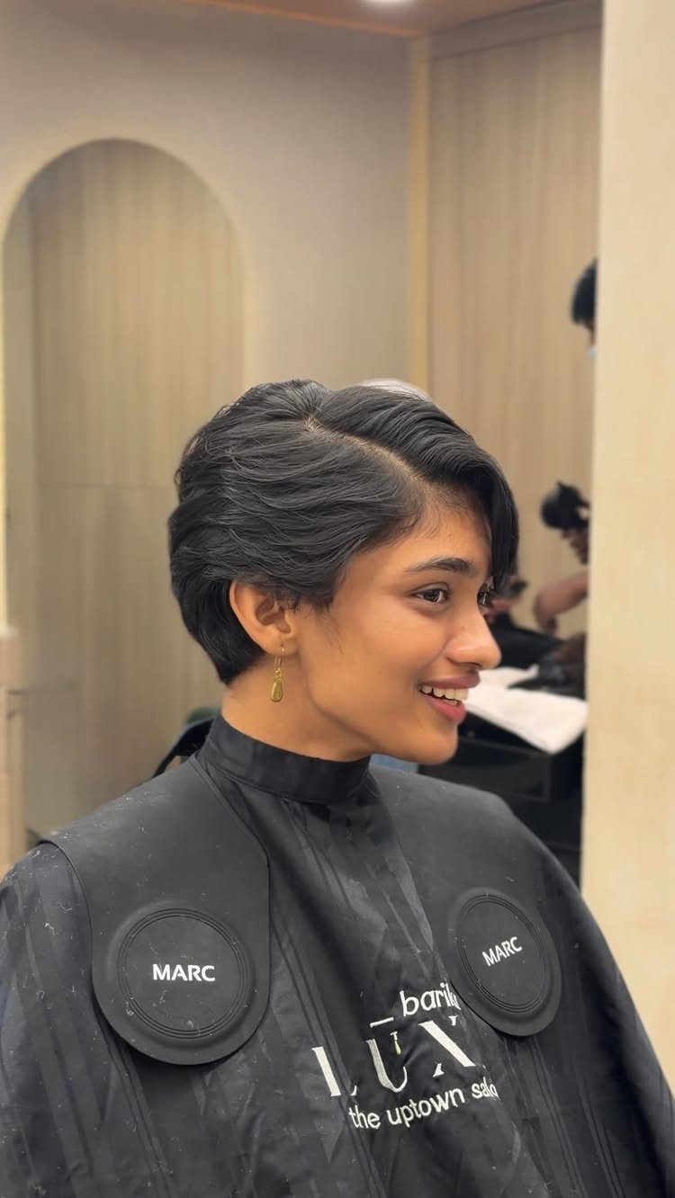 Short, softly layered side-parted haircut shown on a person in a salon chair