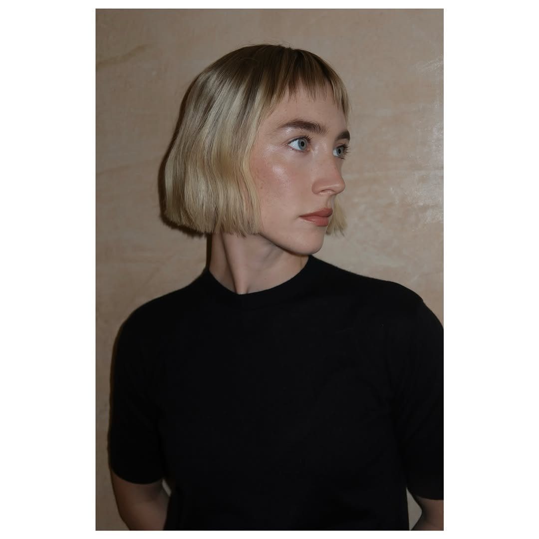 Blonde chin-length bob with short bangs seen in profile against a beige wall