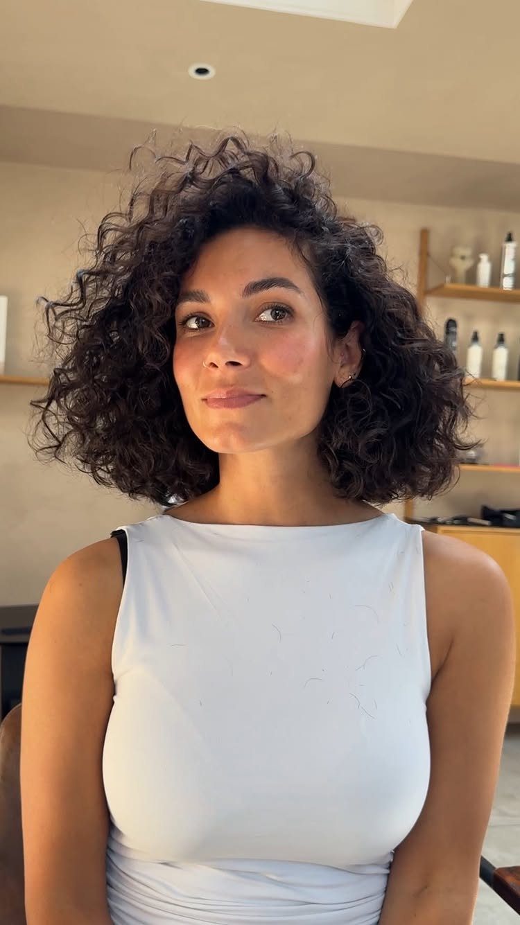 Woman with a voluminous chin-length curly bob in a white sleeveless top