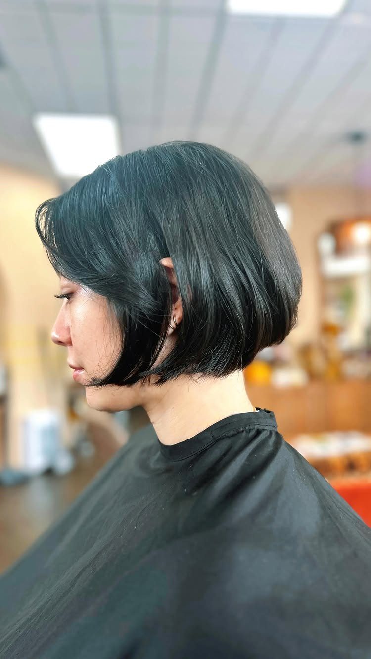 Short dark bob frames a person's jaw in a brightly lit salon