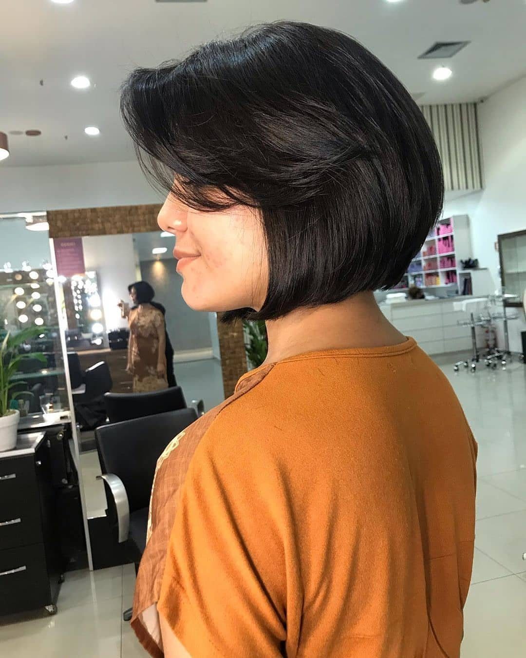 Side-swept black bob frames a woman's face inside a hair salon