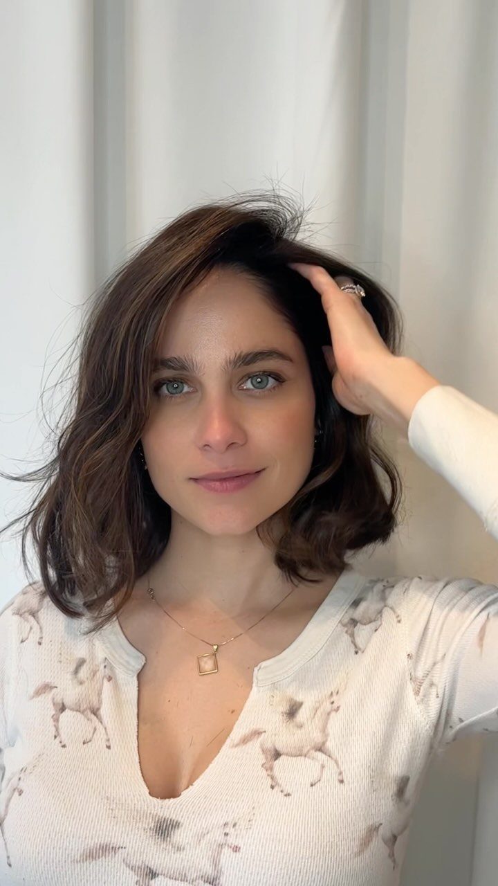 Woman with shoulder-length dark wavy hair touching her hair
