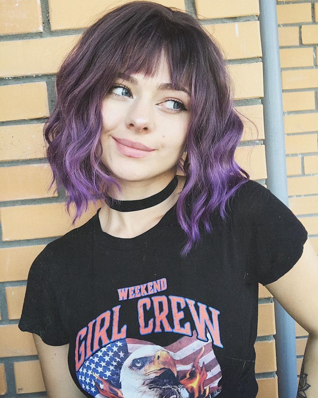 Wavy bob haircut with blunt bangs and purple highlights framing the face