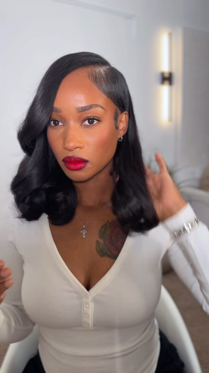 Woman with glossy shoulder-length wavy black bob and deep side part adjusts her hair