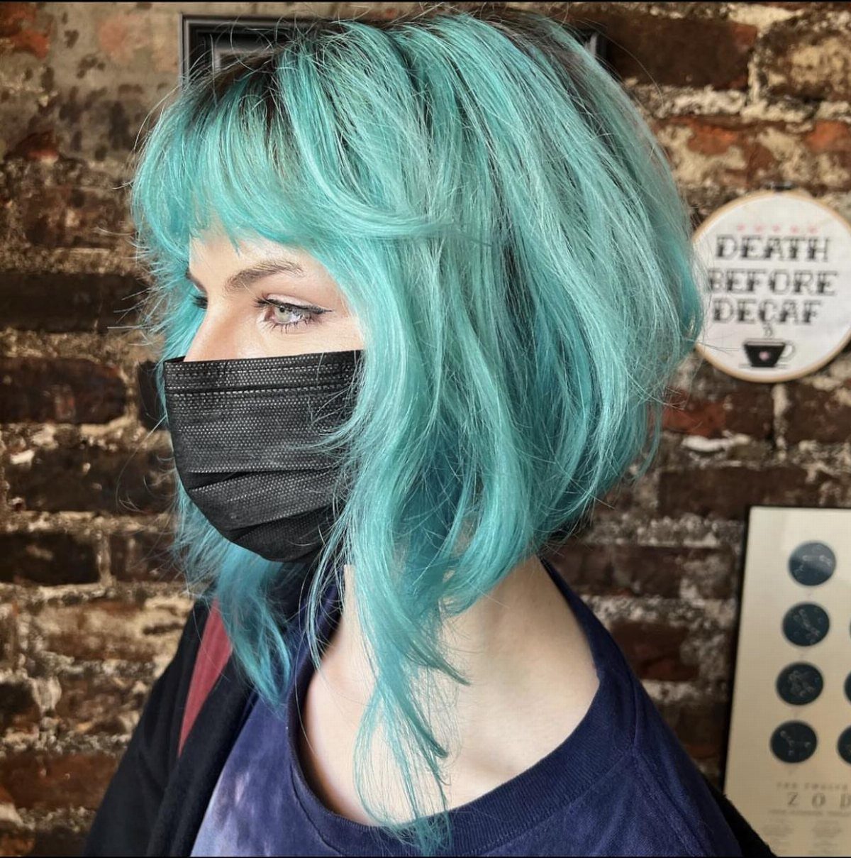 Turquoise bob with layered bangs frames a masked person's face
