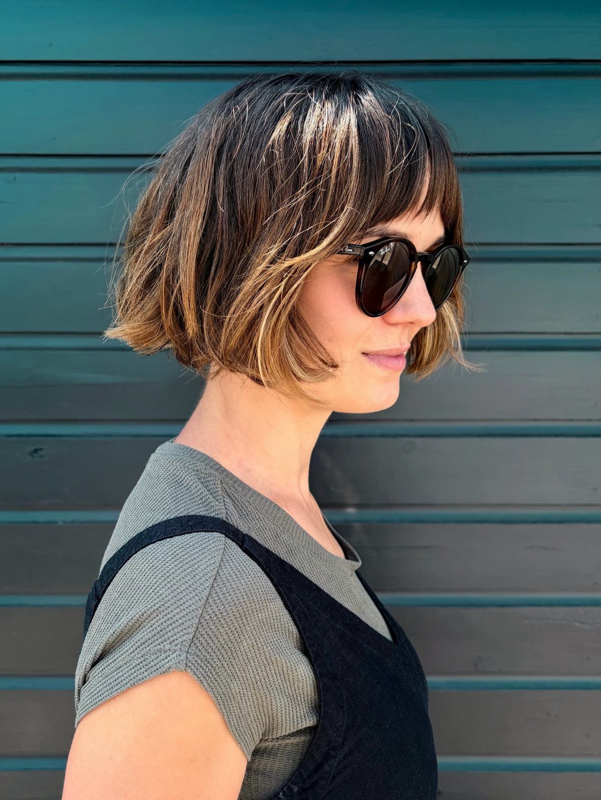 Woman with a highlighted, feathered bob and bangs wearing sunglasses