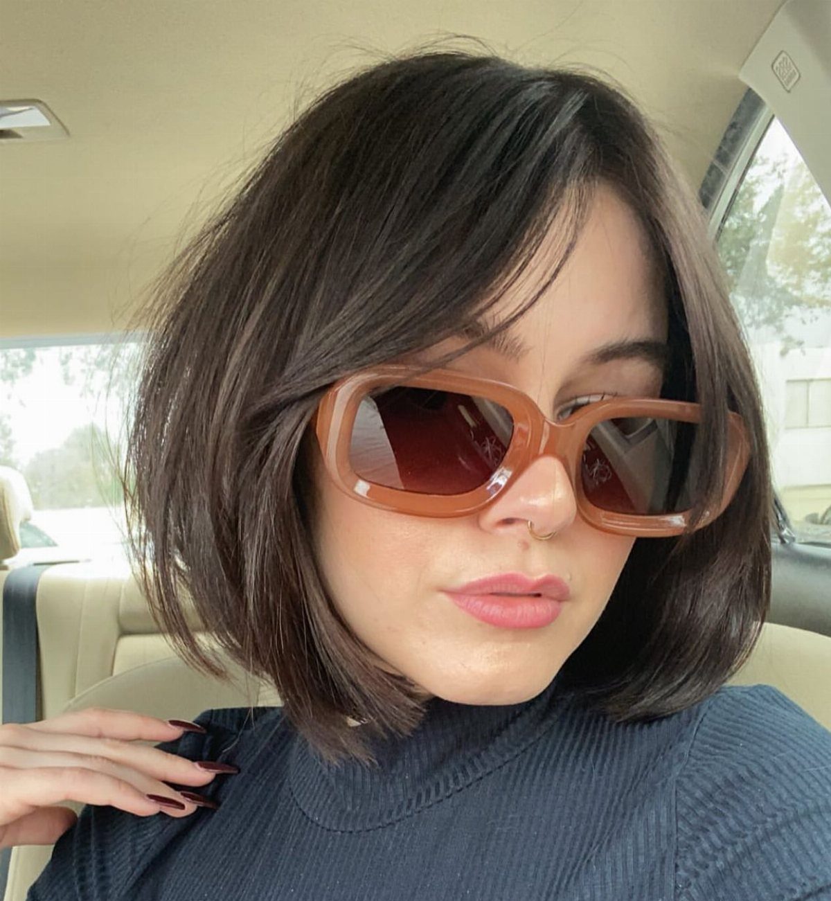 Woman with a layered dark bob and side-swept bangs wearing brown sunglasses
