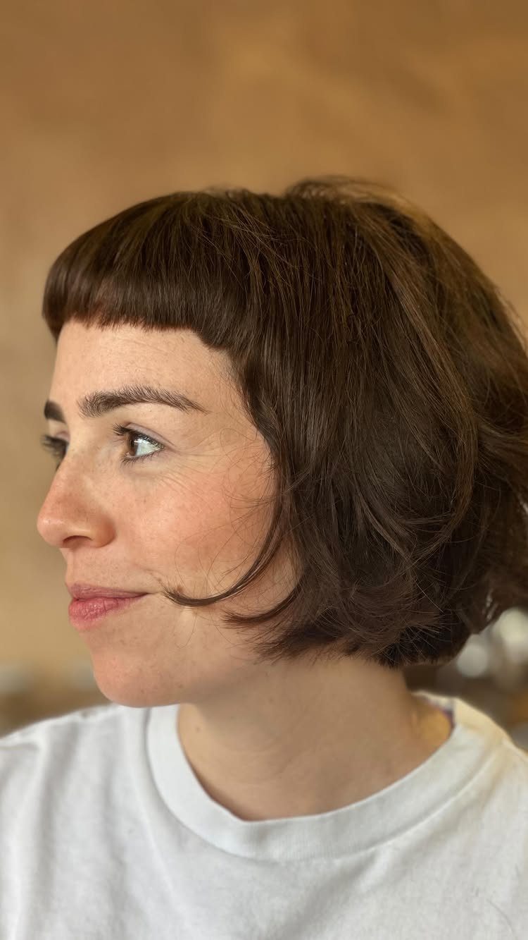 Short dark bob with blunt micro bangs on a person in profile