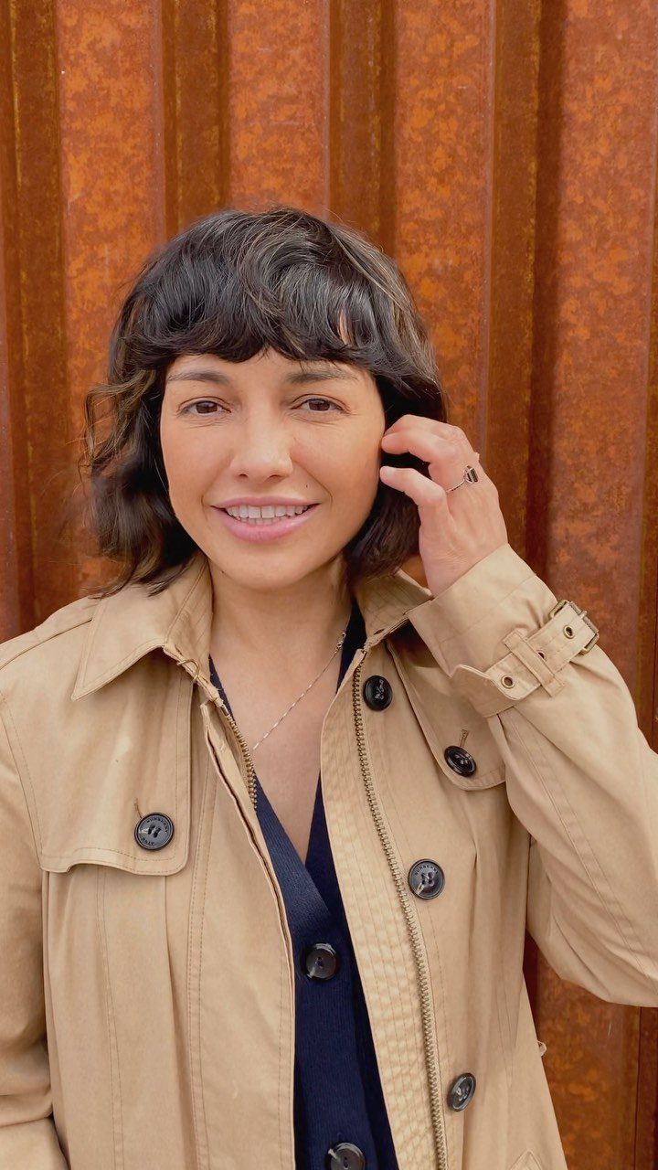 Woman wearing a tousled wavy bob with bangs and a beige jacket