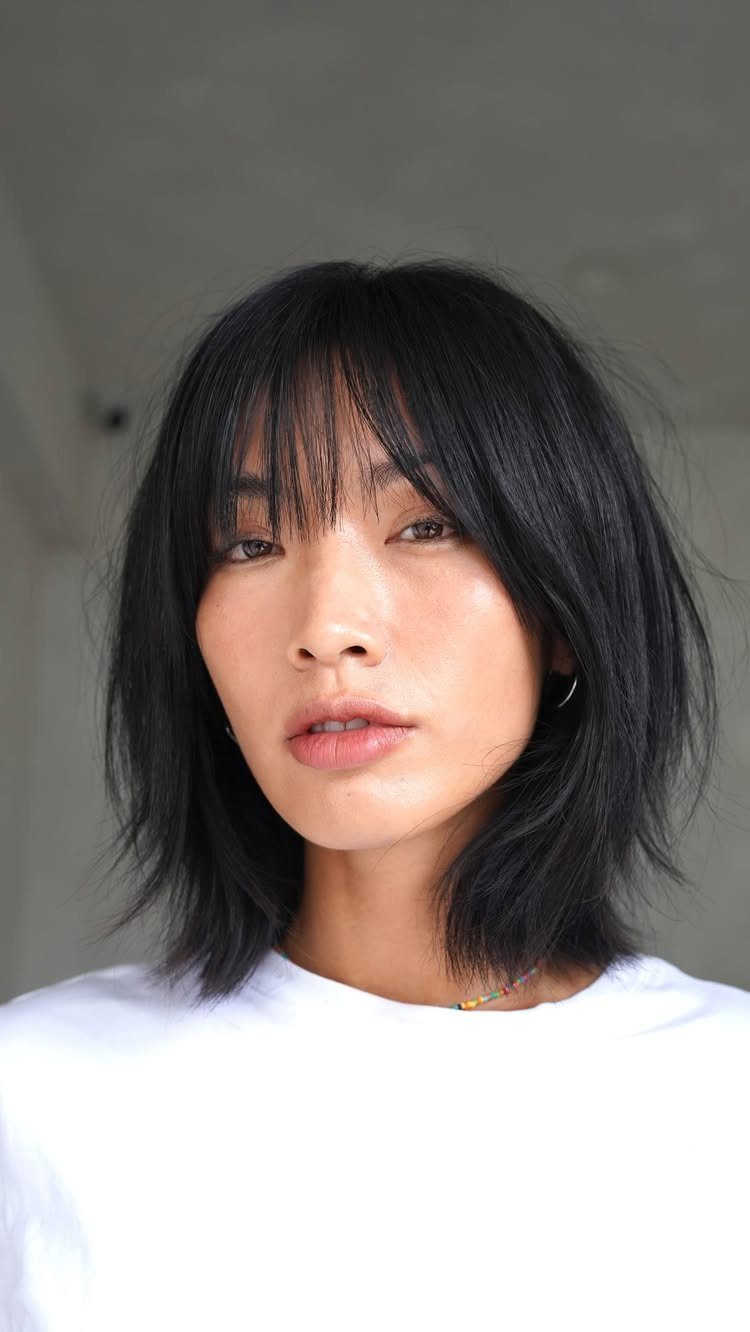 Person with a dark bob haircut and wispy bangs wearing a white top