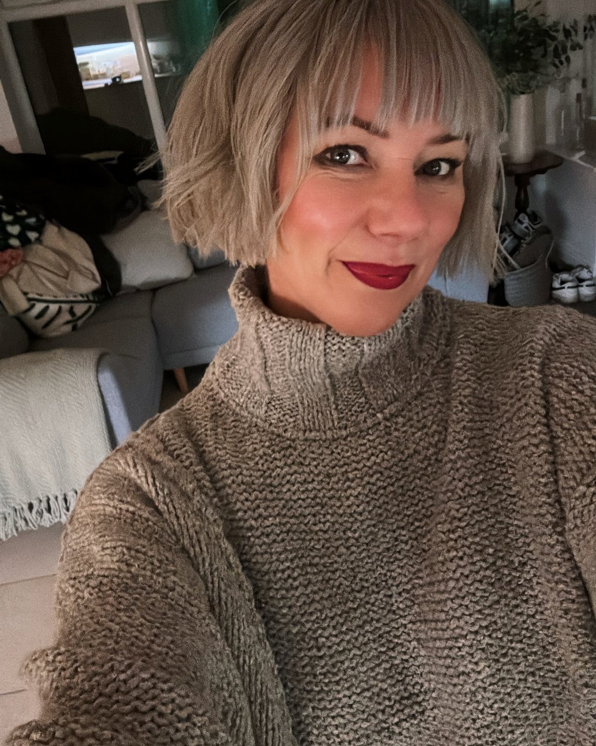 Woman with a short blonde bob and choppy full bangs taking a selfie