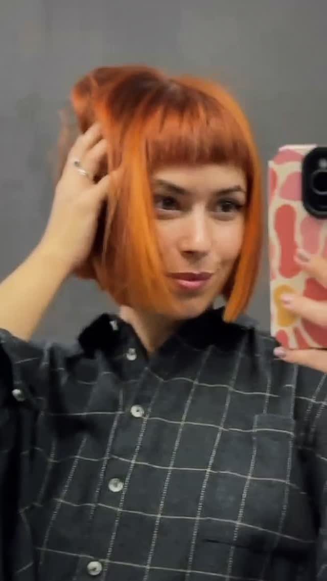 Orange chin-length bob with blunt bangs shown in a mirror selfie