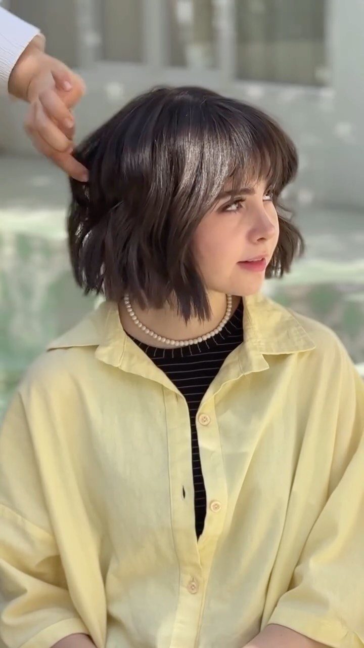 Dark choppy bob with rounded bangs as a hand touches the layered hair