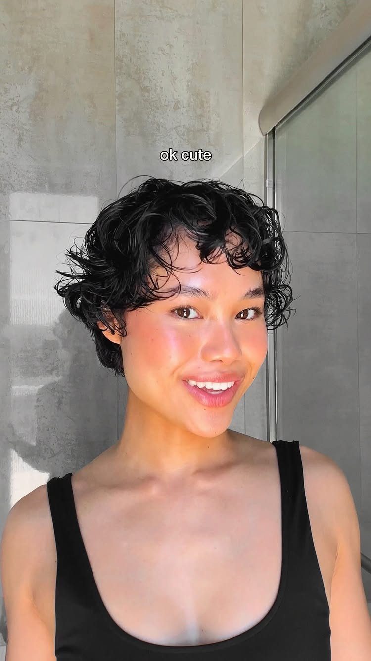 Person smiling with a short curly bob and curls falling across the forehead