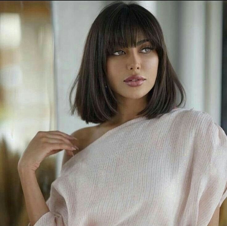 Woman posing with a chin-length dark bob and full straight bangs