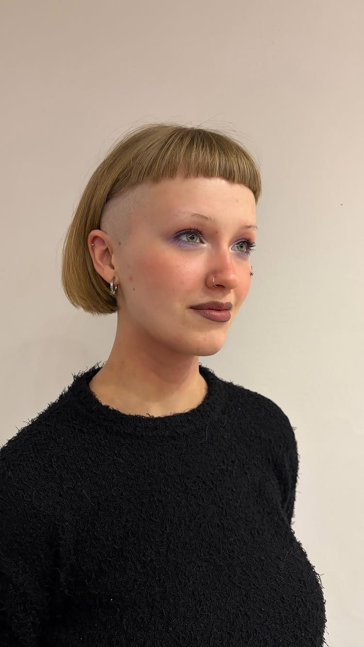 Person with a short light-brown bob, blunt bangs, and shaved sides