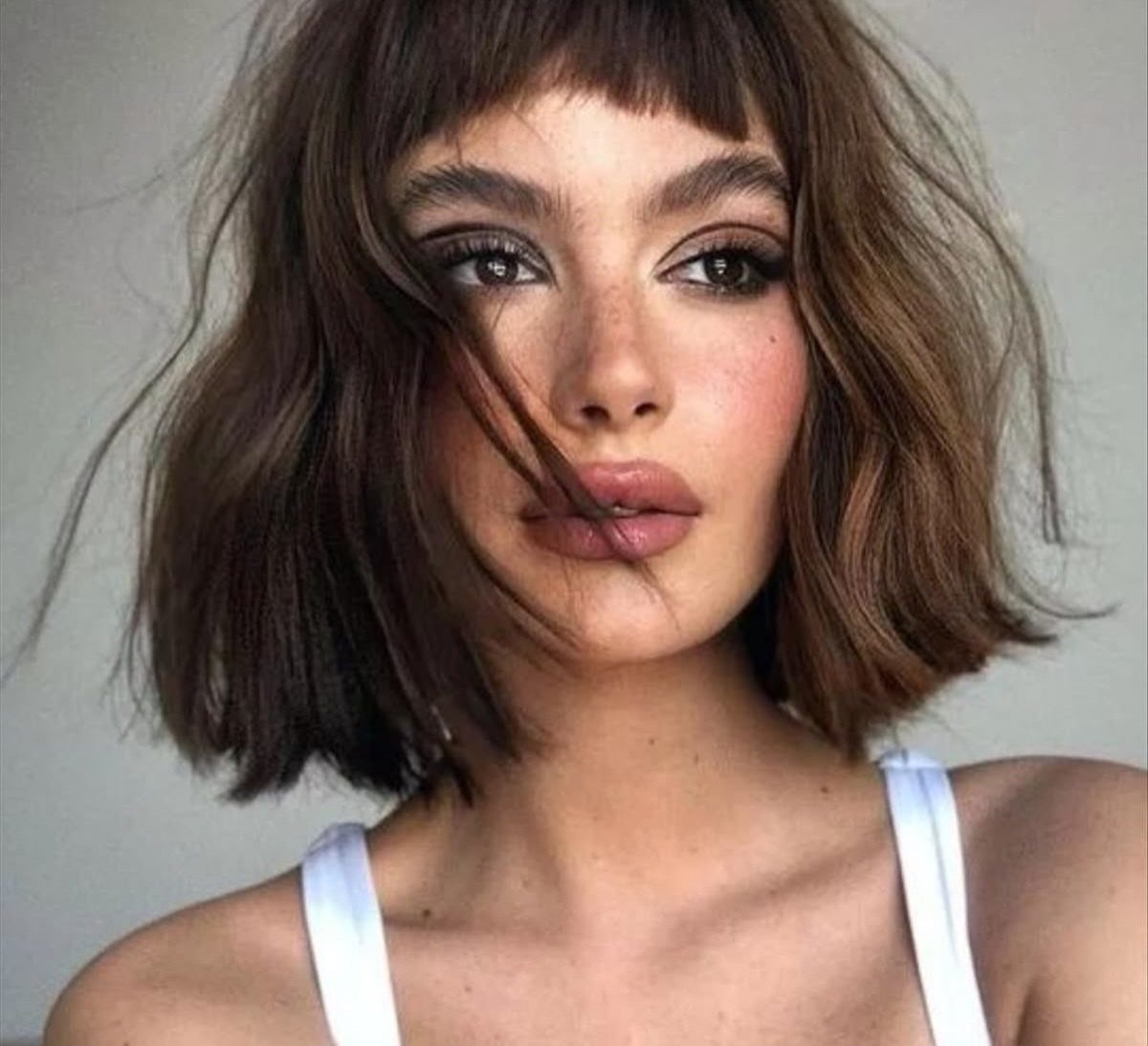Dark brown bob with cropped textured bangs frames a person's face