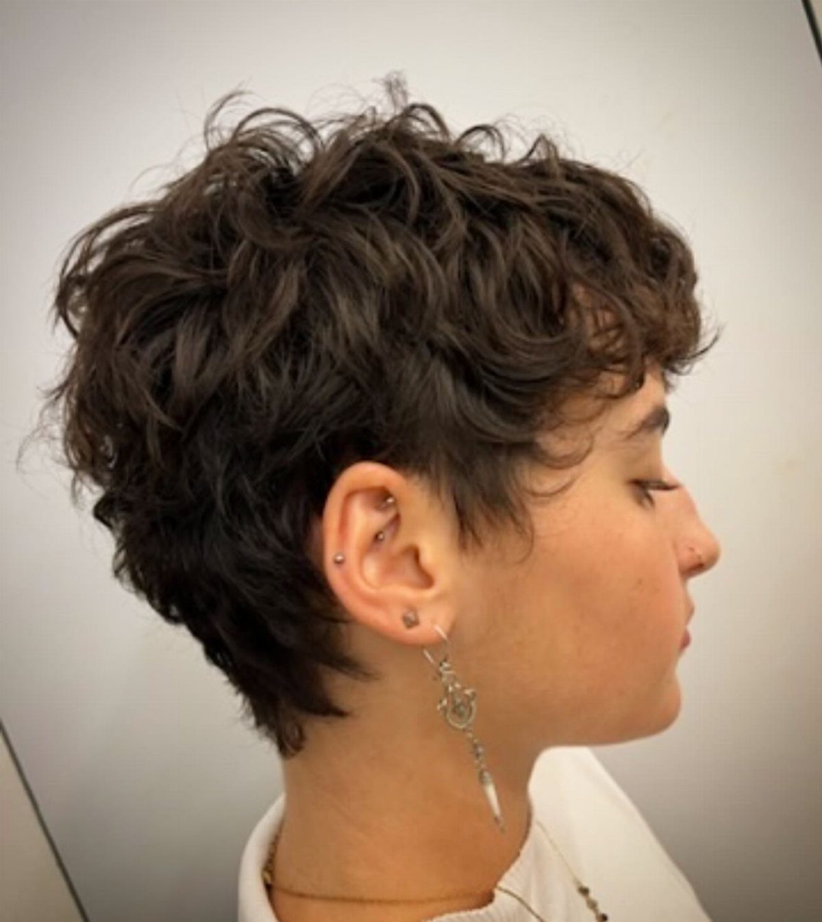 Short dark wavy pixie bob with wispy bangs shown in profile