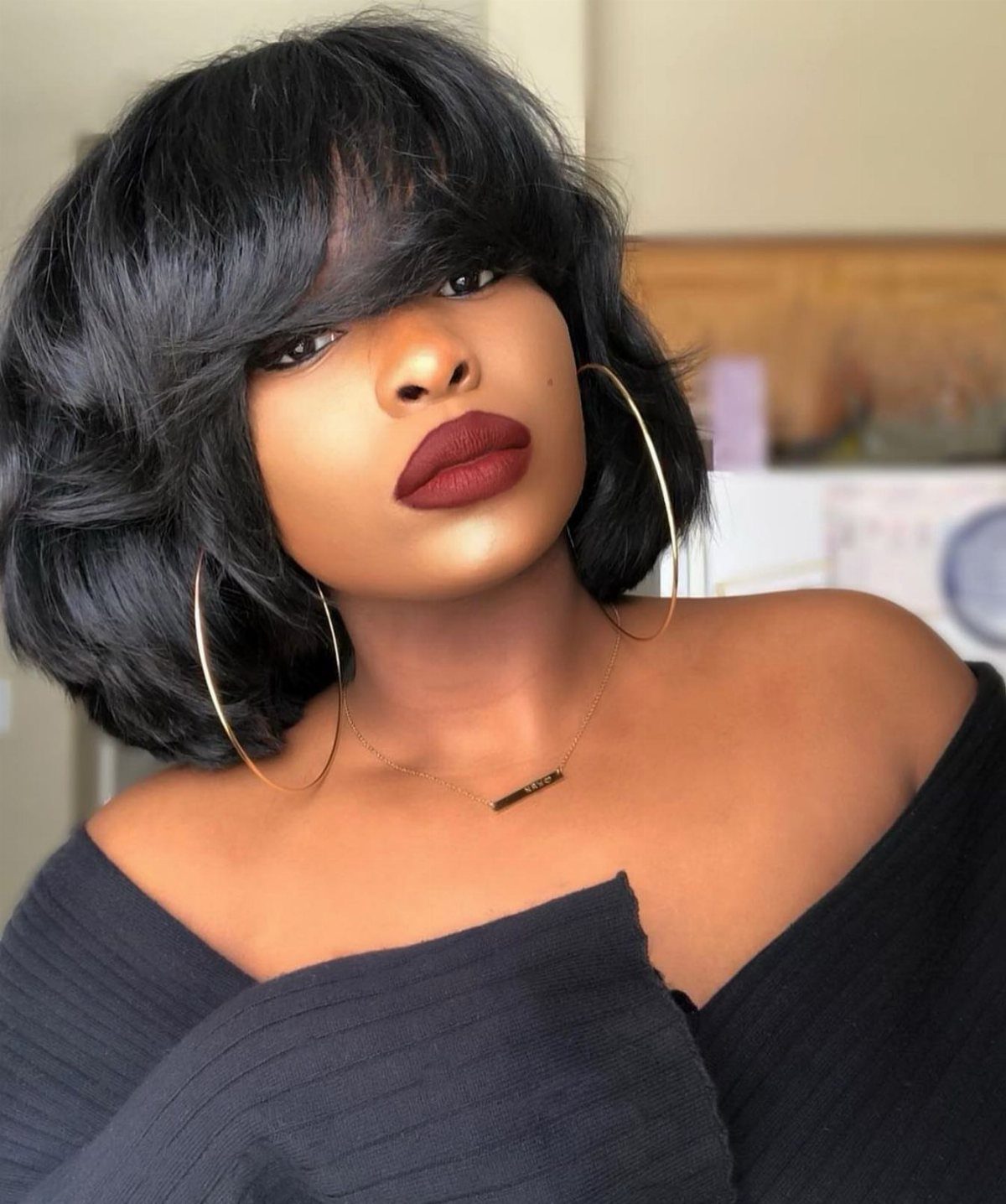 Woman with voluminous black blowout curls, swept bangs, and large hoop earrings