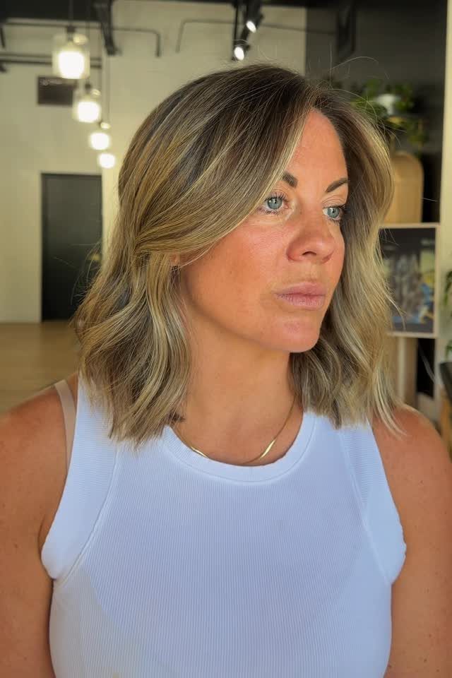 Woman showing a layered blonde lob with darker roots and side-swept bangs