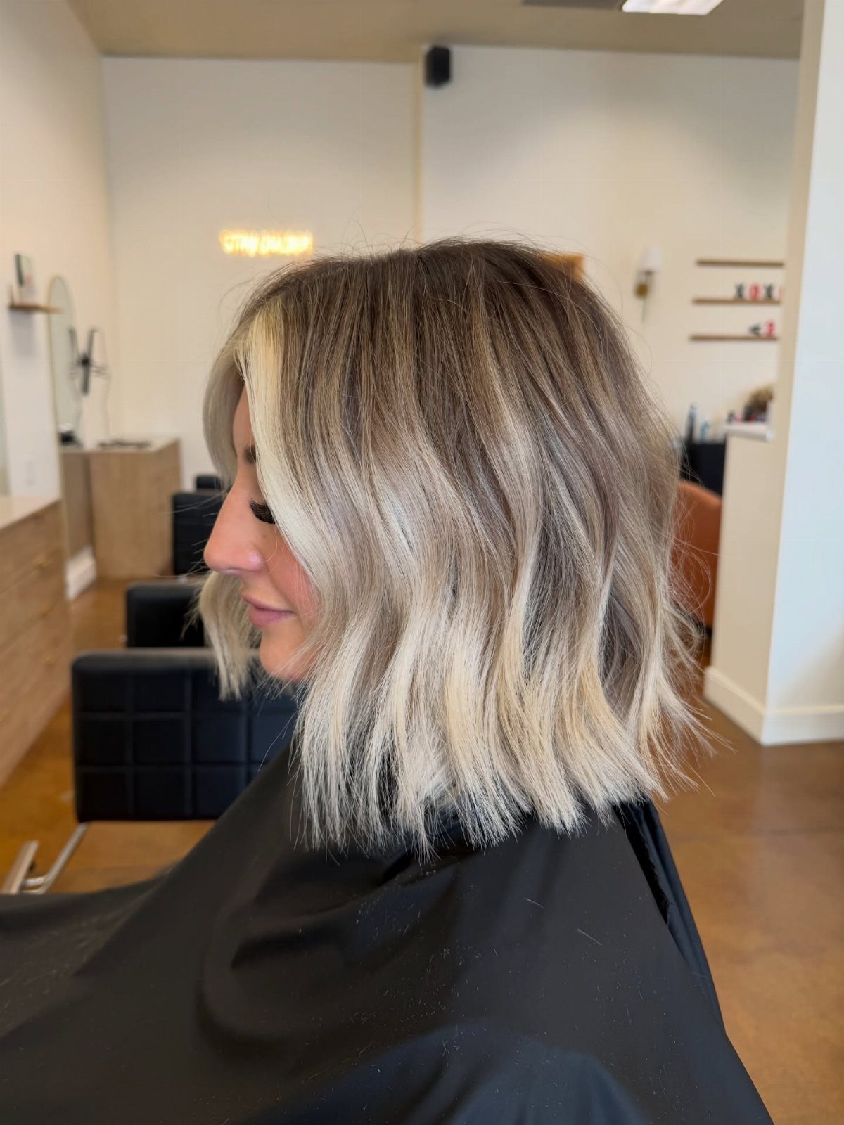 Side-profile woman showing a softly waved, side-swept bleached bob with face-framing layers