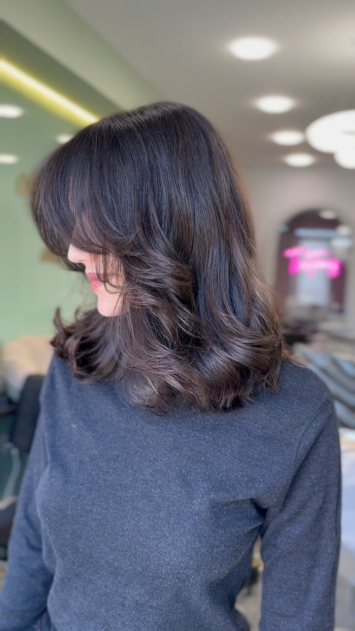 Woman showing a dark shoulder-length bob with swoopy side bangs and curled ends
