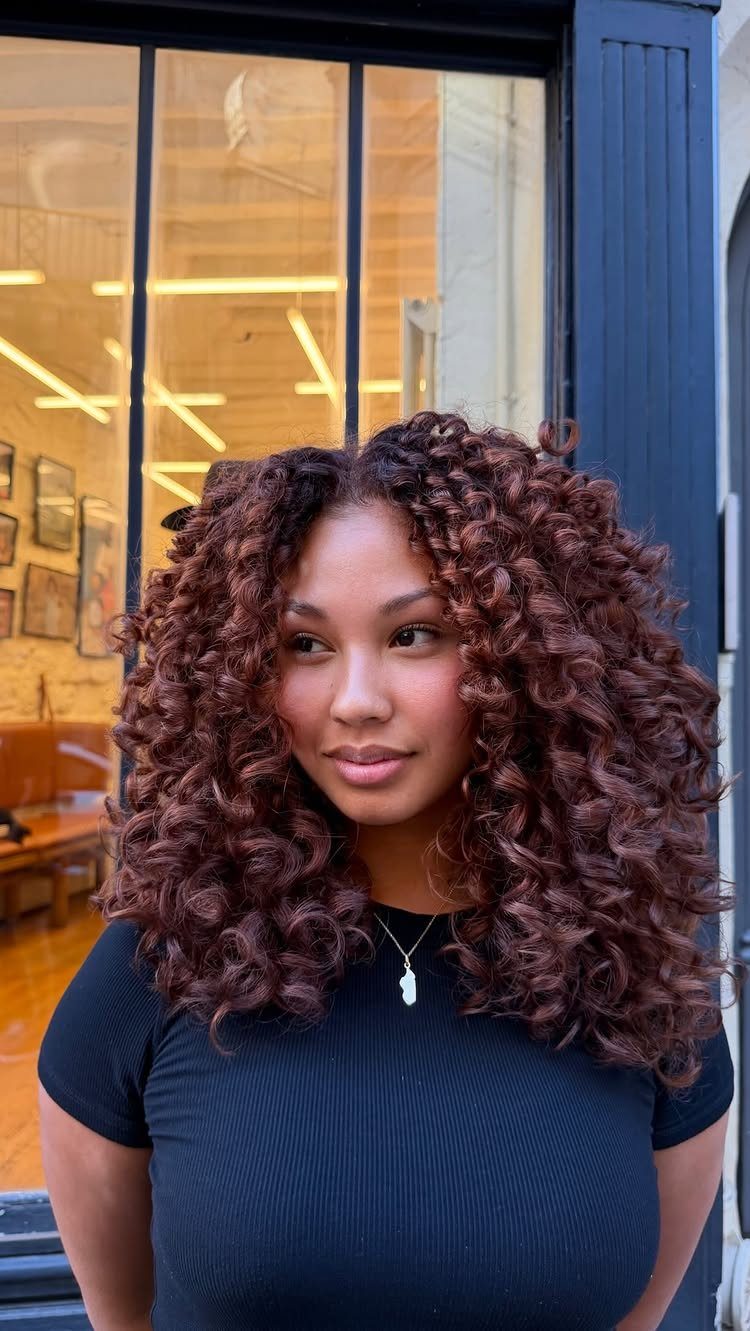 Woman with long, voluminous copper-brown curls standing outside a shop