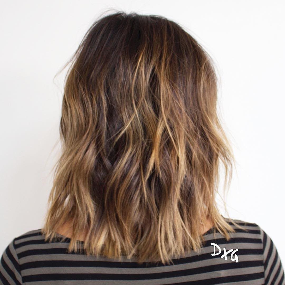Tousled highlighted shoulder-length hair falls in loose, uneven waves over a striped shirt