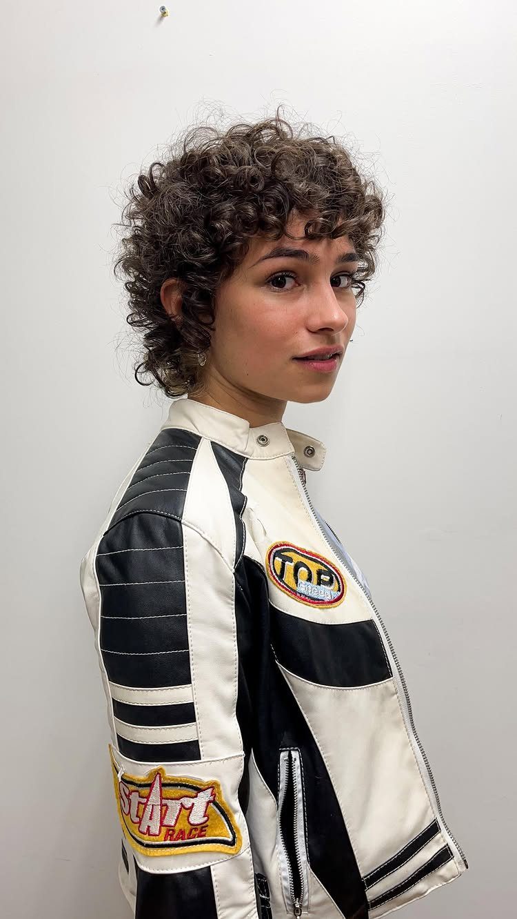 Person with short dark curls wearing a white and black racing jacket