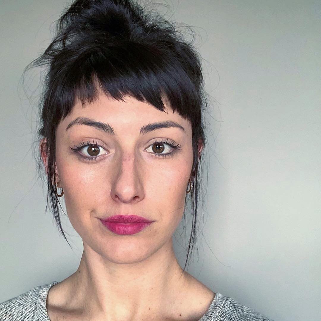 Woman with dark hair in a high bun and short, choppy bangs