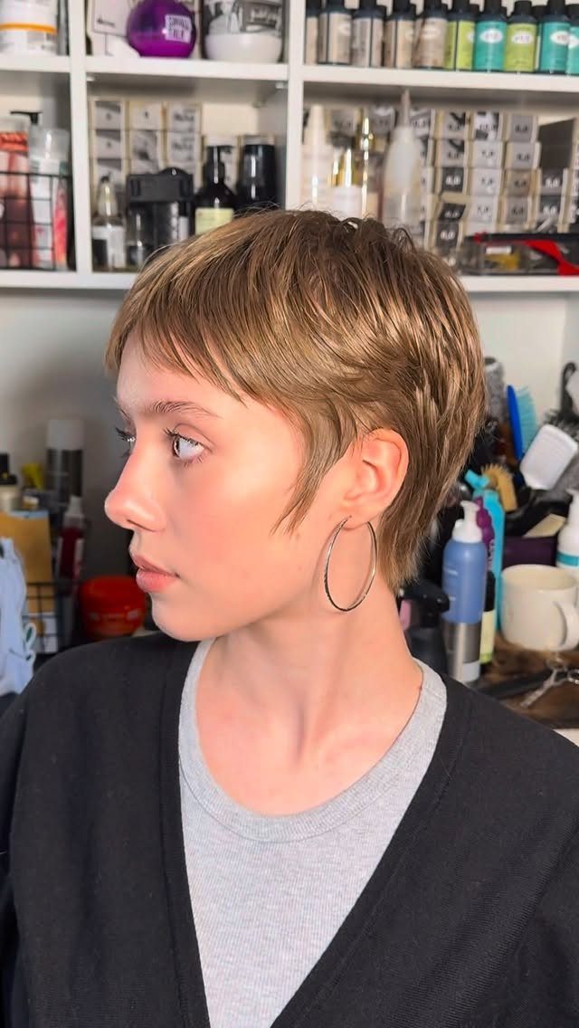 Side-profile person showing a textured light-brown pixie haircut in a salon