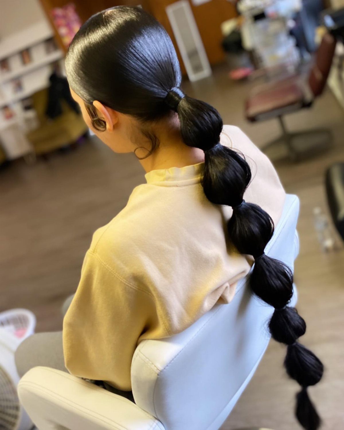 Long black bubble ponytail with rounded sections in a salon chair